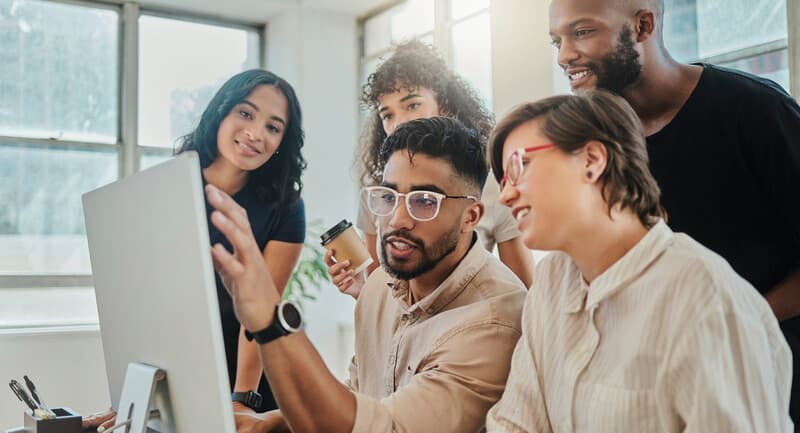 Photo of a teacher and group of students looking thoughtfully at a computer screen