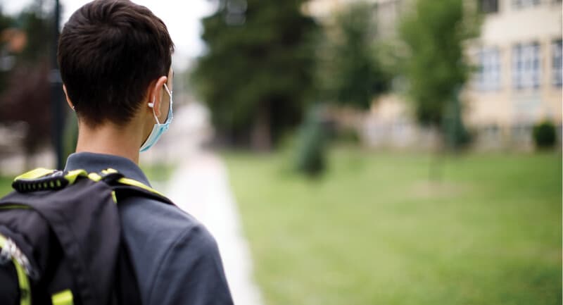 November 2021 Keels thumbnail image: A child with a mask looking in front of a school.