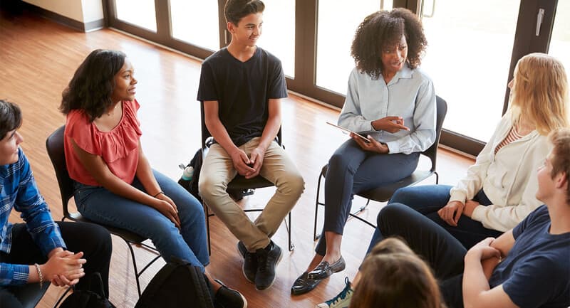 Photo of students seated in a circle talking and listening